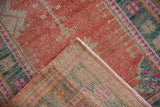 Corner of a vintage distressed Oushak rug folded to show the hand-knotted reverse and pile.