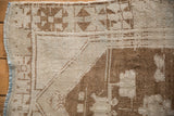 Close-up of the distressed Oushak rug's corner, showing the geometric border and worn, low-pile texture.