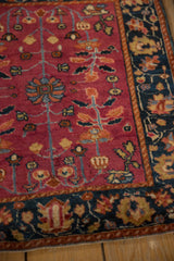 Intricate palmette designs in the dark navy border of a cochineal-field antique Persian rug.