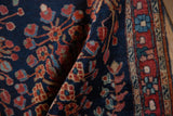Folded antique Farahan Sarouk rug shows blossomed madder red and sky blue motifs on a navy field.