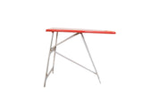 Vintage children's ironing board with a rectangular red top and folding metal legs.