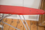 Detailed view of the red metal top on the vintage ironing board, showing authentic patina.