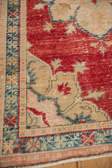 Worn cherry red pile on a distressed Oushak rug corner with a beige and teal border.