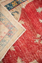 Corner detail of a distressed Oushak rug showing its hand-knotted reverse and worn red pile.