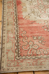 Corner of a distressed Oushak rug with floral and meandering vine borders in dusty rose.