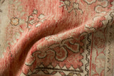 A soft fold on the distressed Oushak rug revealing its time-softened low pile in dusty rose and ivory.