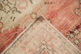 A folded corner of a vintage Oushak rug shows its hand-knotted foundation and worn, dusty rose pile.