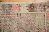 Low pile texture on a distressed Oushak rug corner with a pink and aubergine geometric border.