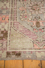 Low-pile texture on a vintage Oushak corner showing its geometric border in aubergine and pink.