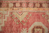 Distressed Oushak corner with a raspberry floral border, geometric motifs, and low-pile texture.
