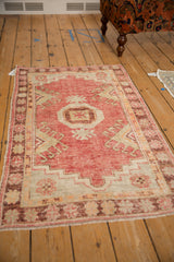 Angled view of a distressed Oushak rug, showing its faded raspberry red and platinum geometric pattern.