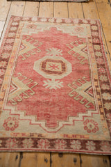 Angled view of a distressed Oushak rug, displaying its pomegranate medallion and faded raspberry red field.