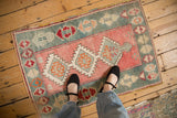 The scale and distressed texture of a small Turkish Oushak rug with rose and teal geometric medallions.