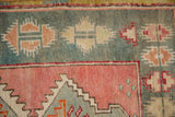 Close-up of the geometric border showing the distressed, hand-knotted pile in faded teal and dusty rose.