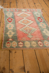 Distressed Oushak rug with geometric medallions in soft rose and teal, seen from a high angle.
