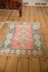 High-angle view of a distressed Oushak rug's dusty rose and faded teal geometric pattern.