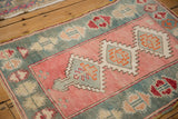 Angled view of a vintage Oushak rug's textured weave and serrated medallions in dusty rose and teal.