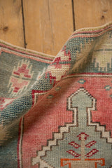 Folded corner of a distressed Oushak rug in dusty rose and teal, showing its even, hand-knotted pile.