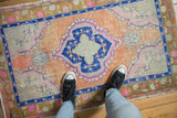 Curvilinear medallion of a distressed Oushak rug, showing cantaloupe, cobalt, and magenta tones underfoot.