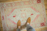 A person's view of a distressed vintage Oushak rug, showing its scale and worn texture.
