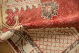 A folded corner on a distressed Oushak rug reveals its worn texture and lattice corner design.