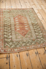 Distressed vintage Melas rug close-up: olive green border, ribboned vines, terra cotta roses.