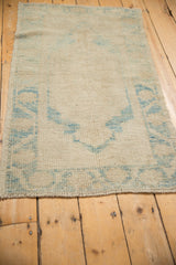 Distressed Oushak rug corner, showing heavy abrash, fringed edge, and sky blue arabesque motif.