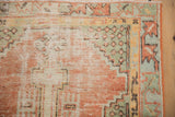 Distressed Oushak rug corner, featuring dusty blush and jade green seeded patterns, showing low pile.