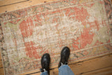 A person's view of a distressed vintage Oushak rug's soft blush and mint green tones.