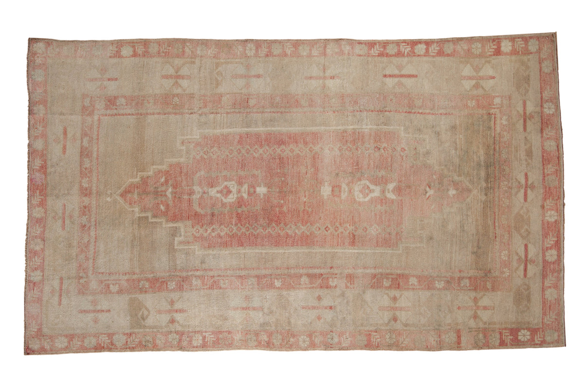Vintage distressed Oushak carpet with pink geometric designs and wide borders on a dusty beige field.
