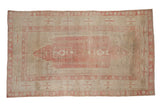 Vintage distressed Oushak carpet with pink geometric designs and wide borders on a dusty beige field.