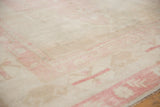 Angled close-up of the distressed Oushak's short pile and soft pink geometric floral border.