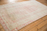 Low-angle view of a distressed Oushak carpet highlighting its short pile and faded pink design.