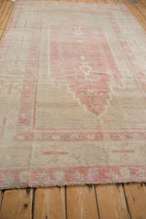 Angled view showing the low pile and abrashes of a distressed pink and ivory Oushak carpet.