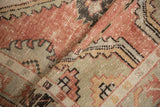Distressed pile texture of a vintage Oushak rug, with dusty rose, seafoam, and brown geometric patterns.