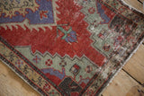 Worn corner of a vintage Oushak rug showing distressed texture and faded cherry red and slate blue hues.