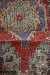 Close-up of a distressed Oushak rug's fold showing low-pile texture in red and slate blue.