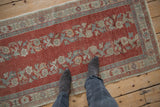 Distressed Oushak runner: feet on brick red field, dusty blue floral borders.