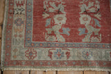 Distressed Oushak rug corner, brick red field, dusty blue serrated leaf border, and fringe.