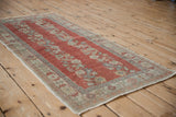 Distressed brick red pile and faded blue floral border on this Oushak rug edge.