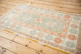 Angled view showing the soft, low-pile texture of a vintage distressed Oushak rug in seafoam and rust.