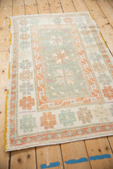 Angled view of a distressed Oushak rug with a faded seafoam green and pale rust geometric design.