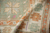 Folded corner of a distressed Oushak rug revealing its soft, low-pile texture in seafoam and pale rust.