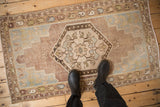 Distressed vintage Oushak rug corner showing pale sage spandrel, dusty mauve field, and meandering vine border.