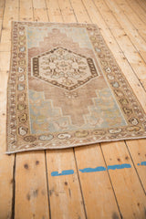 Distressed Oushak rug corner with meandering vine, boteh borders, dusty mauve, sage, and blue.