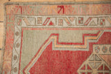 Textured low pile and geometric borders of a vintage Oushak rug in dusty rose, greige, and cherry red.