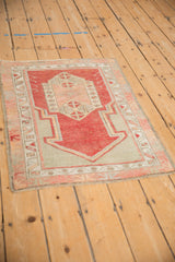 Angled view of a distressed Oushak prayer rug with a faded cherry red geometric design.