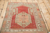 Angled view of a vintage Oushak prayer rug in distressed cherry red and dusty greige tones.