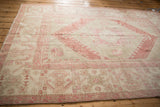 Soft, worn texture of a distressed Turkish Oushak carpet with faded pink and ivory geometric patterns.