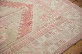 Angled view of a vintage Oushak's border with distressed pink cloudband motifs on an ivory field.
